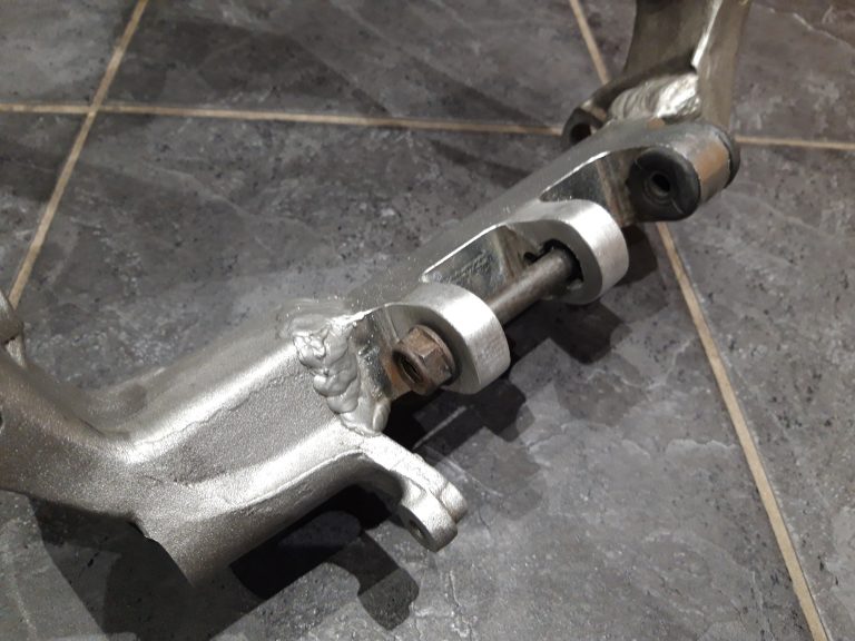 A close-up view of a metal mechanical part with welded joints and a rusted bolt, placed on a tiled floor.