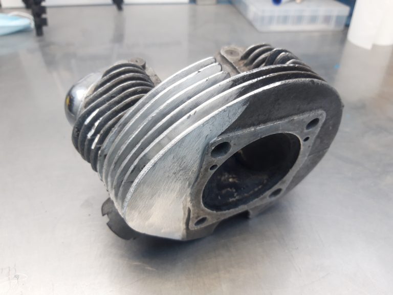 A aluminium cylinder head fin repair with an open central chamber sits on a stainless steel work surface.