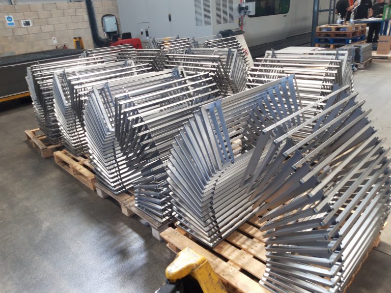 Stacks of metal frames or brackets are neatly arranged on wooden pallets inside an industrial facility or workshop.
