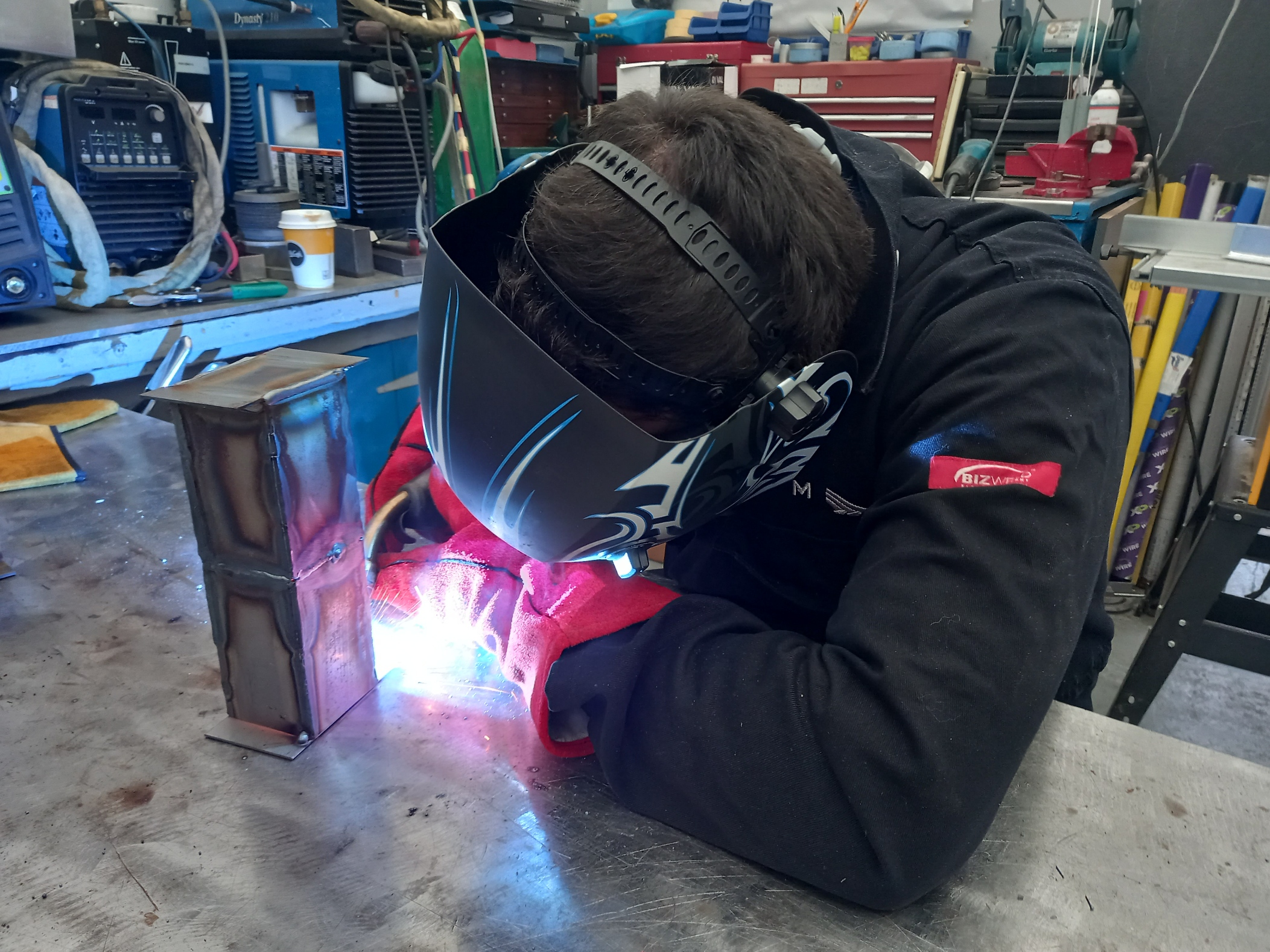 Red and black welding student welding with sparks