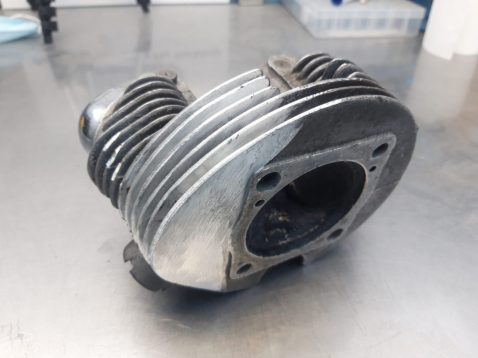 A aluminium cylinder head fin repair with an open central chamber sits on a stainless steel work surface.