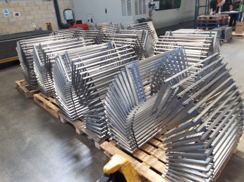 Stacks of metal frames are neatly arranged on wooden pallets in an industrial warehouse setting.